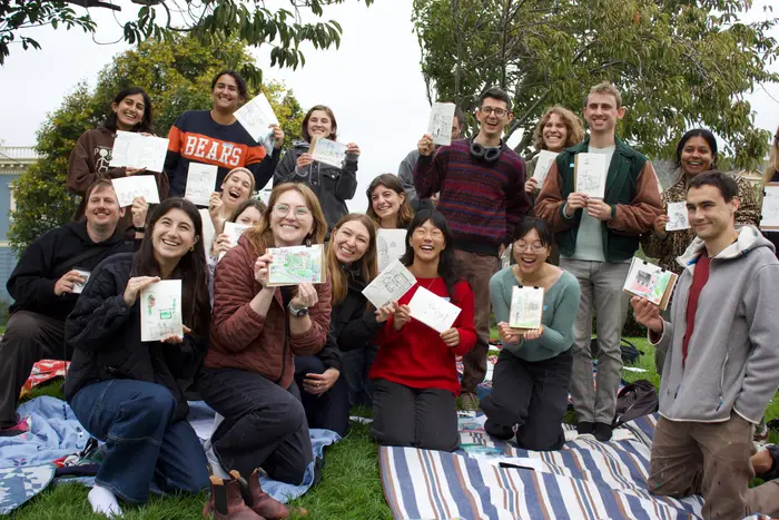 Smiling urban sketching workshop participants holding up their finished drawings together in the park.