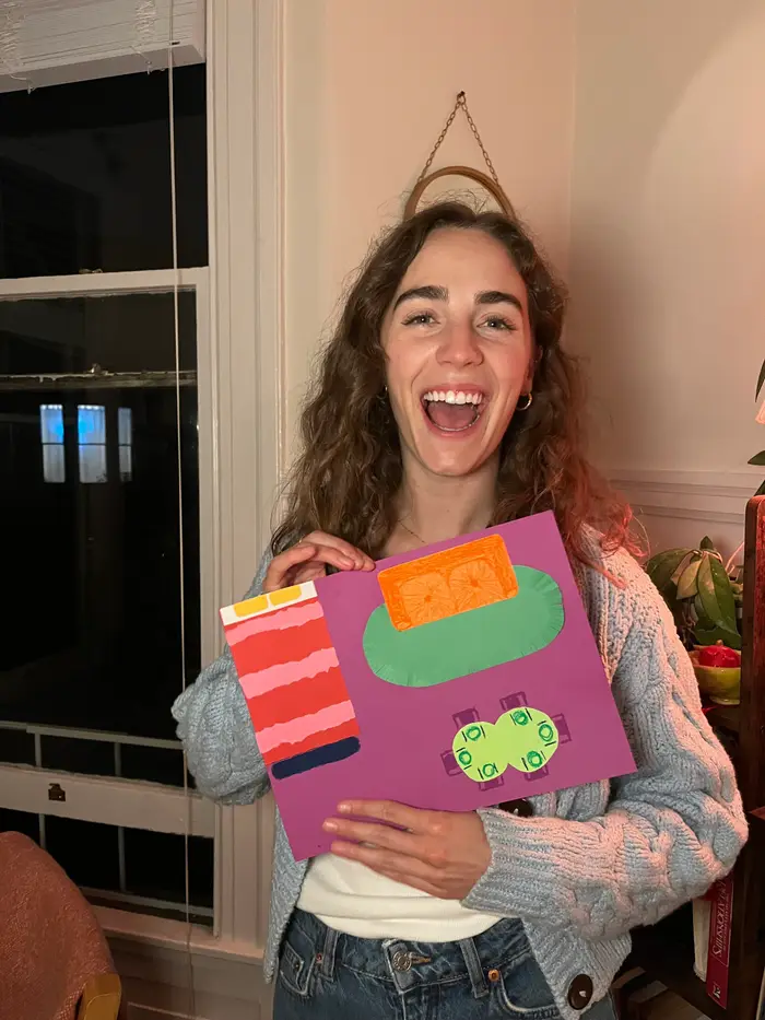 A smiling participant holding a colorful still life collage on purple paper.