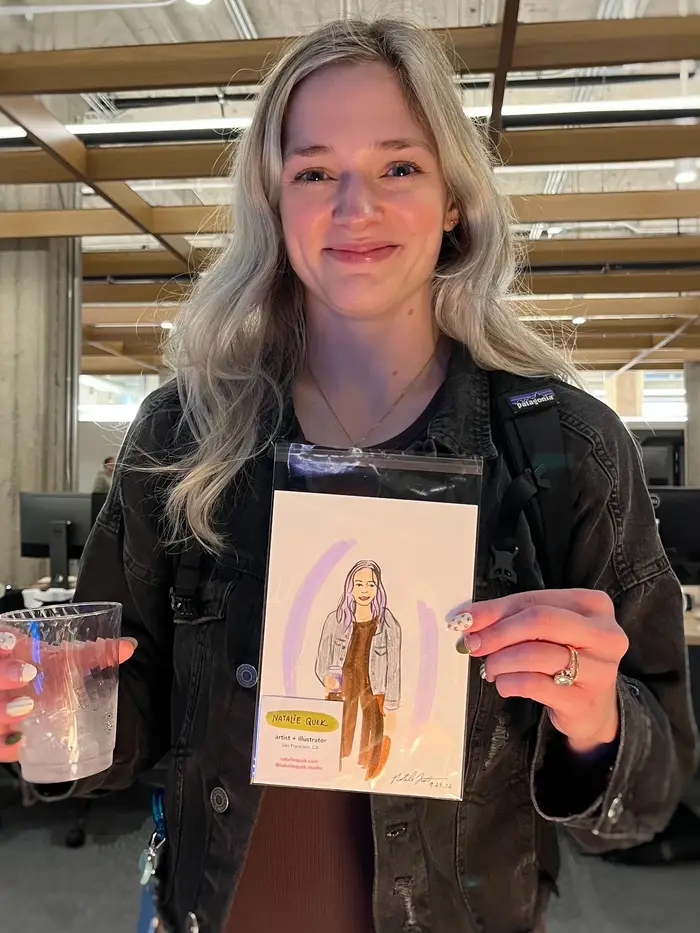 Guest in a dark denim jacket holding her colorful illustrated portrait